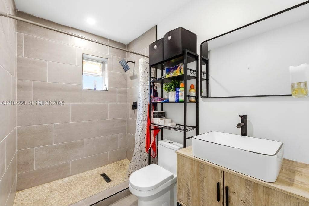 Bathroom featuring a walk-in shower with large-format wall tile and a pebble-stone floor, a floating vanity with a rectangular vessel sink, a matte black faucet, and a wall-mounted rectangular mirror