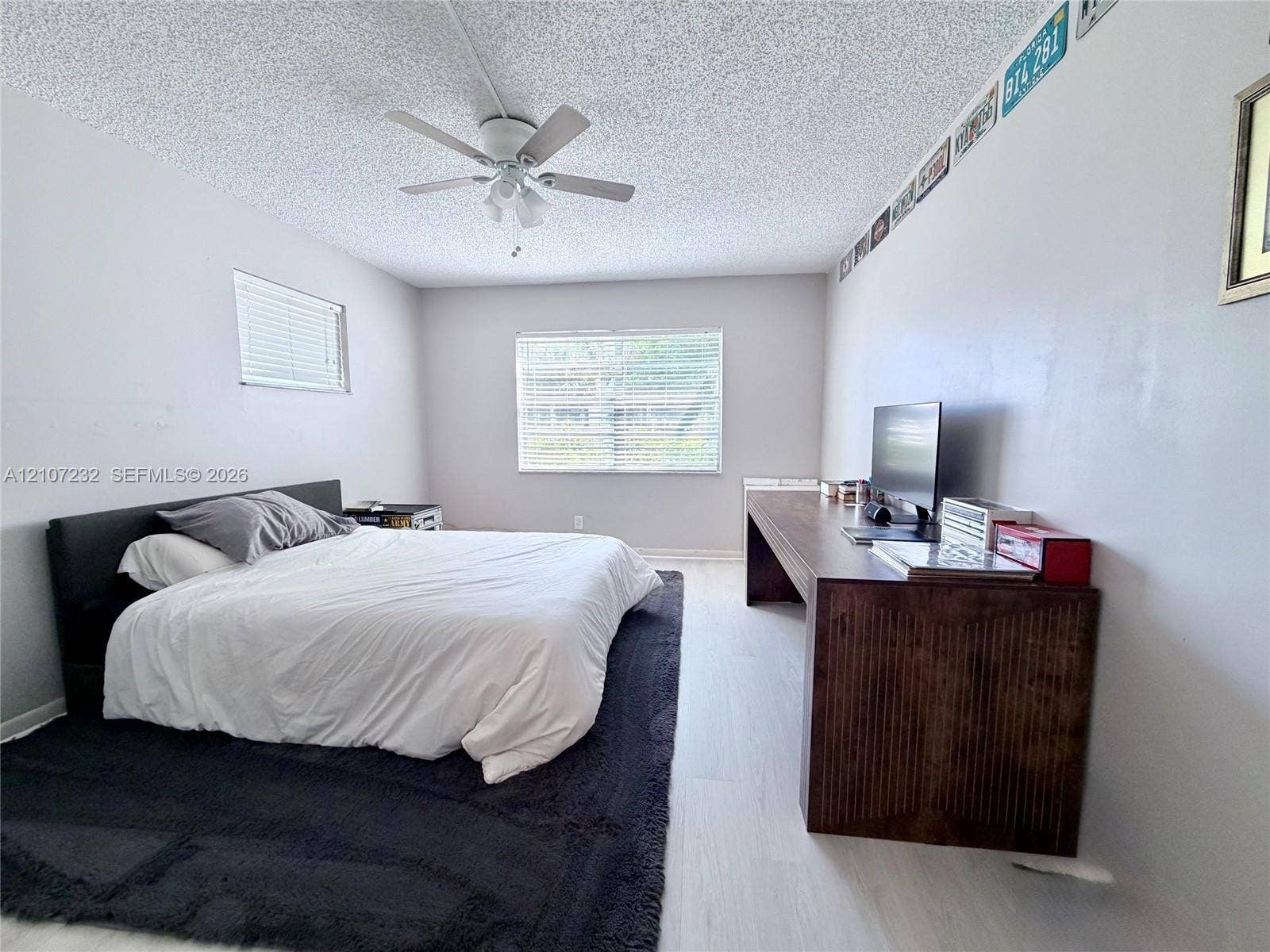 Wood-finish flooring, dual windows with horizontal blinds, and a ceiling-mounted fan with integrated lighting