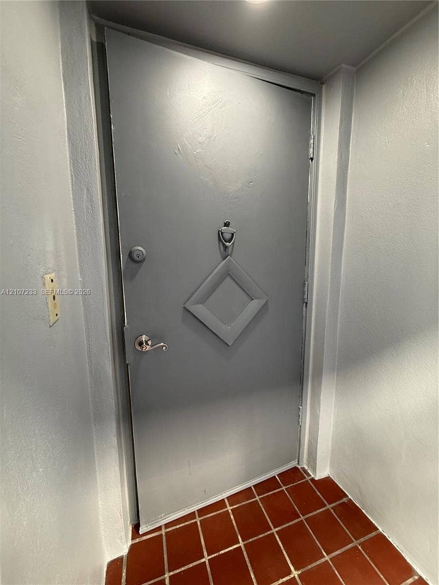 215 SE 3rd Avenue, #102D, Hallandale Beach, Hallandale Beach, FL 33009 Solid door featuring a geometric diamond-shaped panel, chrome finish lever handle, and a decorative metal door knocker, set against red ceramic floor tiling
