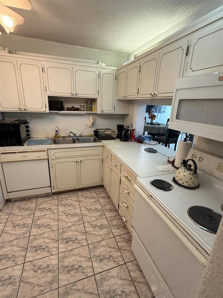 215 SE 3rd Avenue, #102D, Hallandale Beach, Hallandale Beach, FL 33009 Kitchen featuring solid-surface countertops, white cabinetry with recessed-panel doors, a dual-basin sink, an over-the-range microwave, and ceramic tile flooring