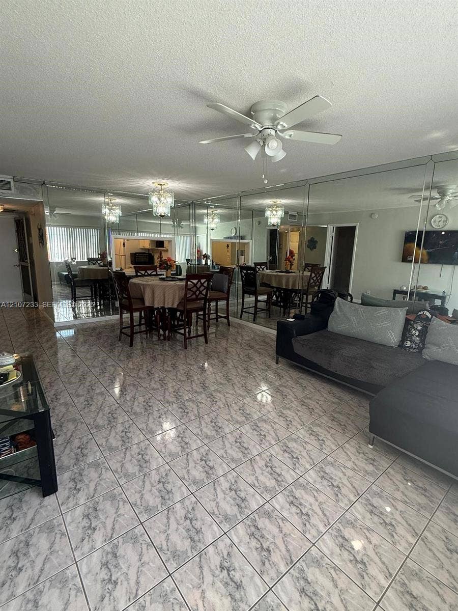 215 SE 3rd Avenue, #102D, Hallandale Beach, Hallandale Beach, FL 33009 Spacious room featuring floor-to-ceiling mirrored walls, patterned tile flooring, a multi-blade ceiling fan, and a built-in crystal-style chandelier