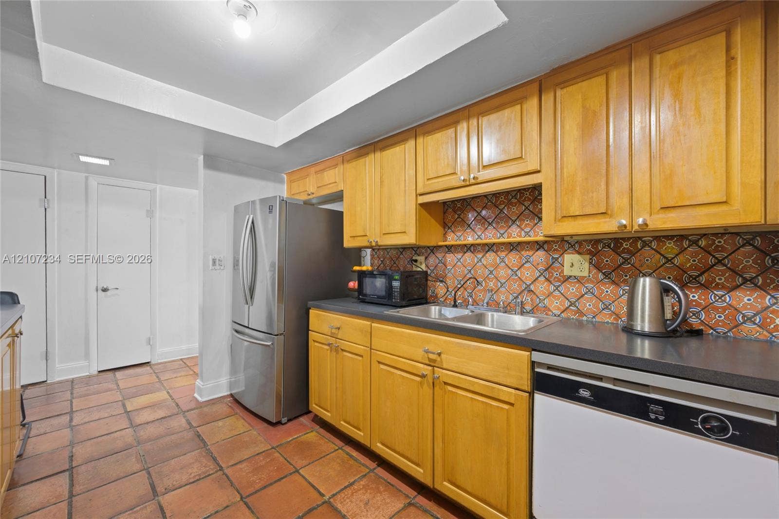 13507 NE 24th Court, North Miami, FL 33181 Kitchen featuring wood cabinetry, patterned tile backsplash, stainless steel refrigerator, dual-basin sink, and terracotta floor tiling