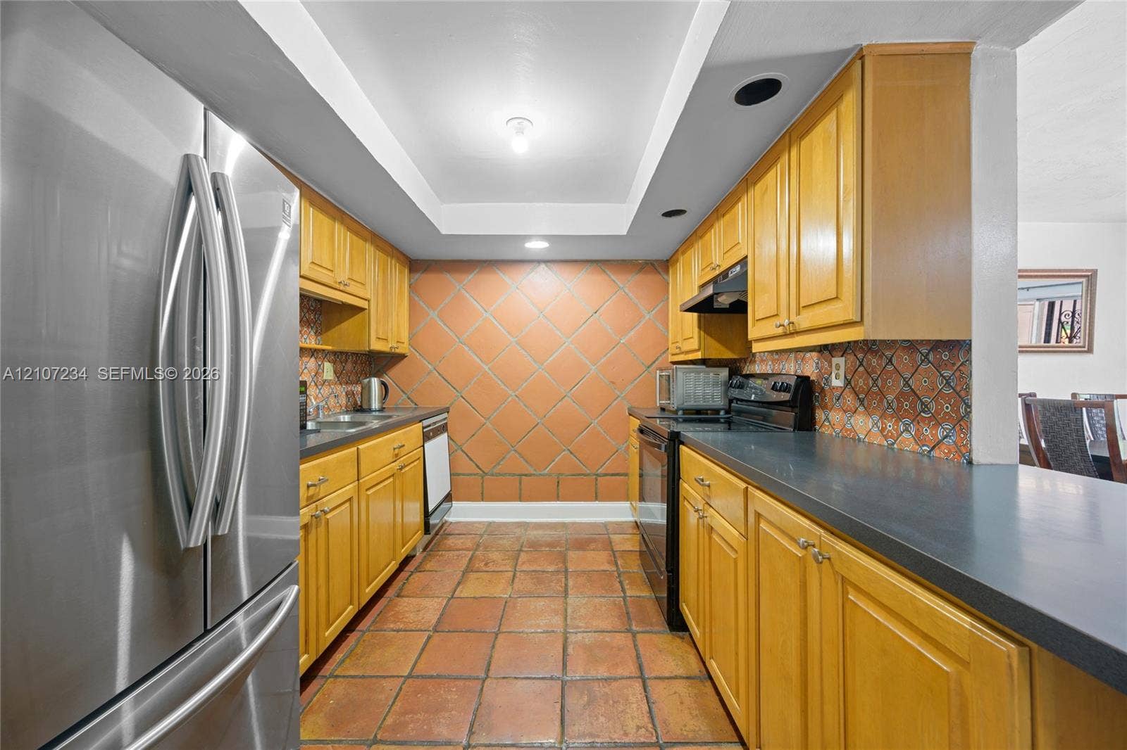13507 NE 24th Court, North Miami, FL 33181 Kitchen featuring wood cabinetry, solid-surface countertops, terra-cotta tile flooring, patterned ceramic tile backsplash, and stainless-steel appliances