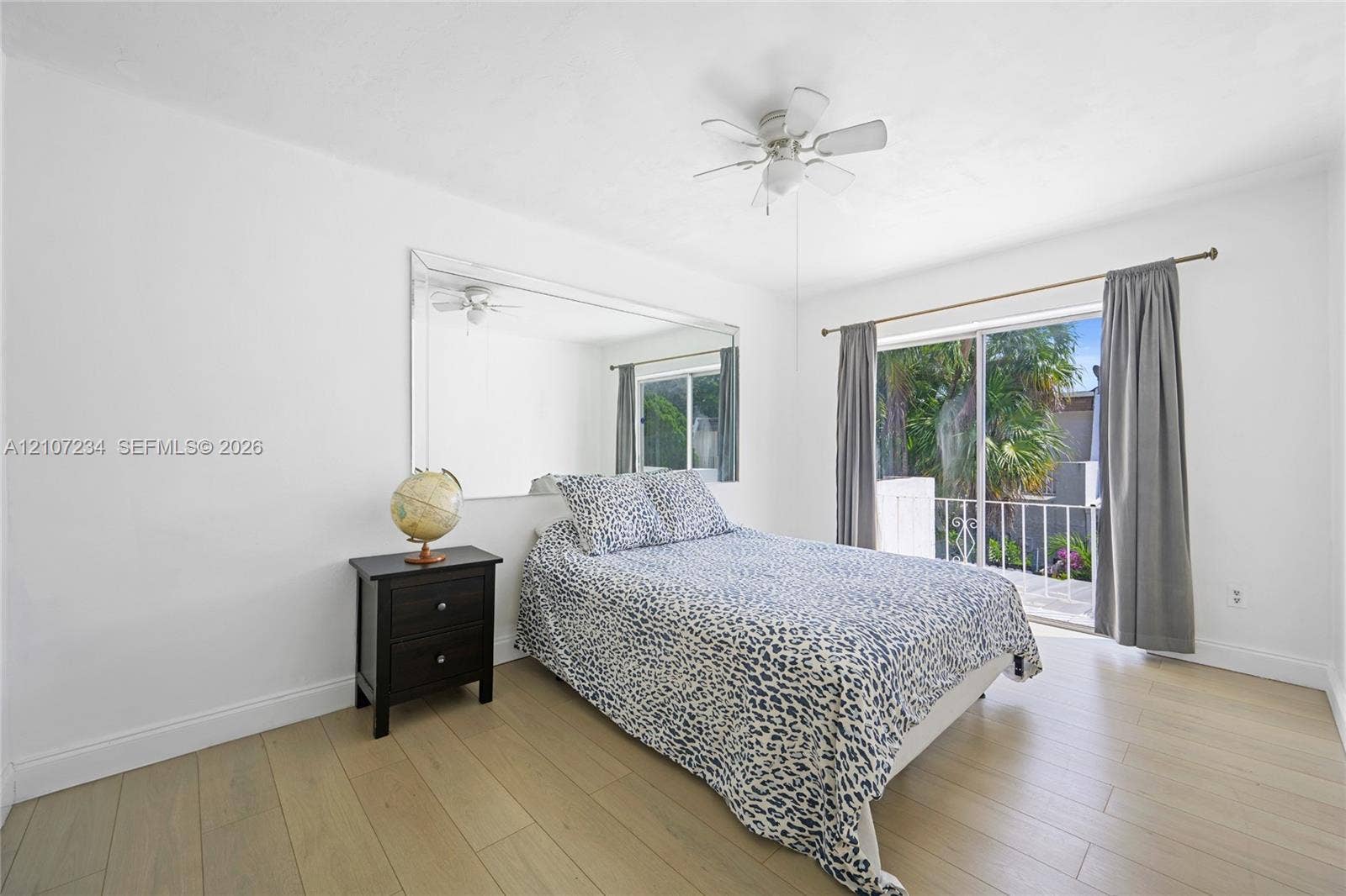 13507 NE 24th Court, North Miami, FL 33181 Wood-finish flooring, large wall-mounted mirror, ceiling fan with integrated light fixture, and sliding glass door with exterior railing