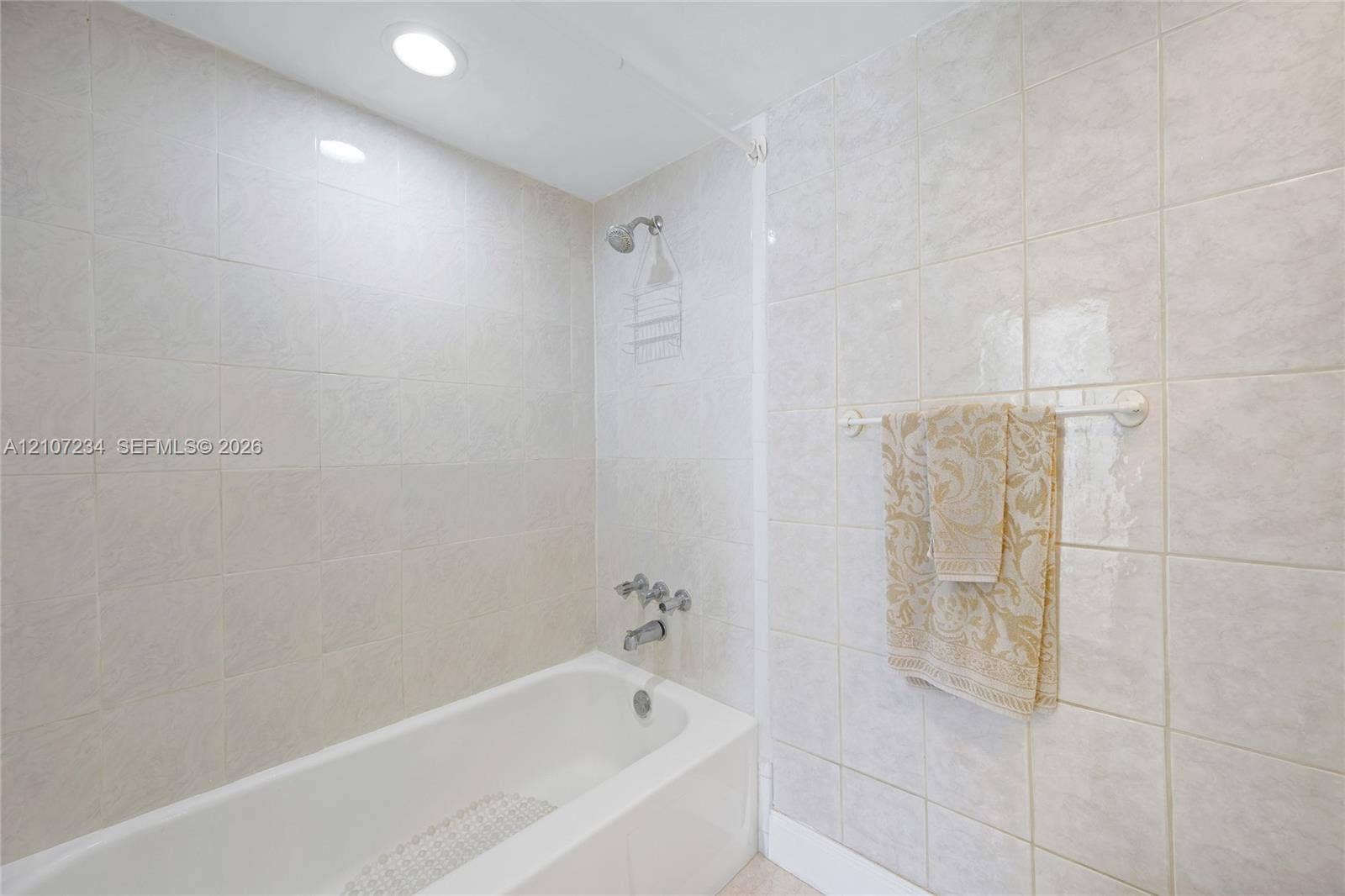 13507 NE 24th Court, North Miami, FL 33181 Full-height wall tiling surrounding a white bathtub with a built-in shower faucet and recessed ceiling lighting