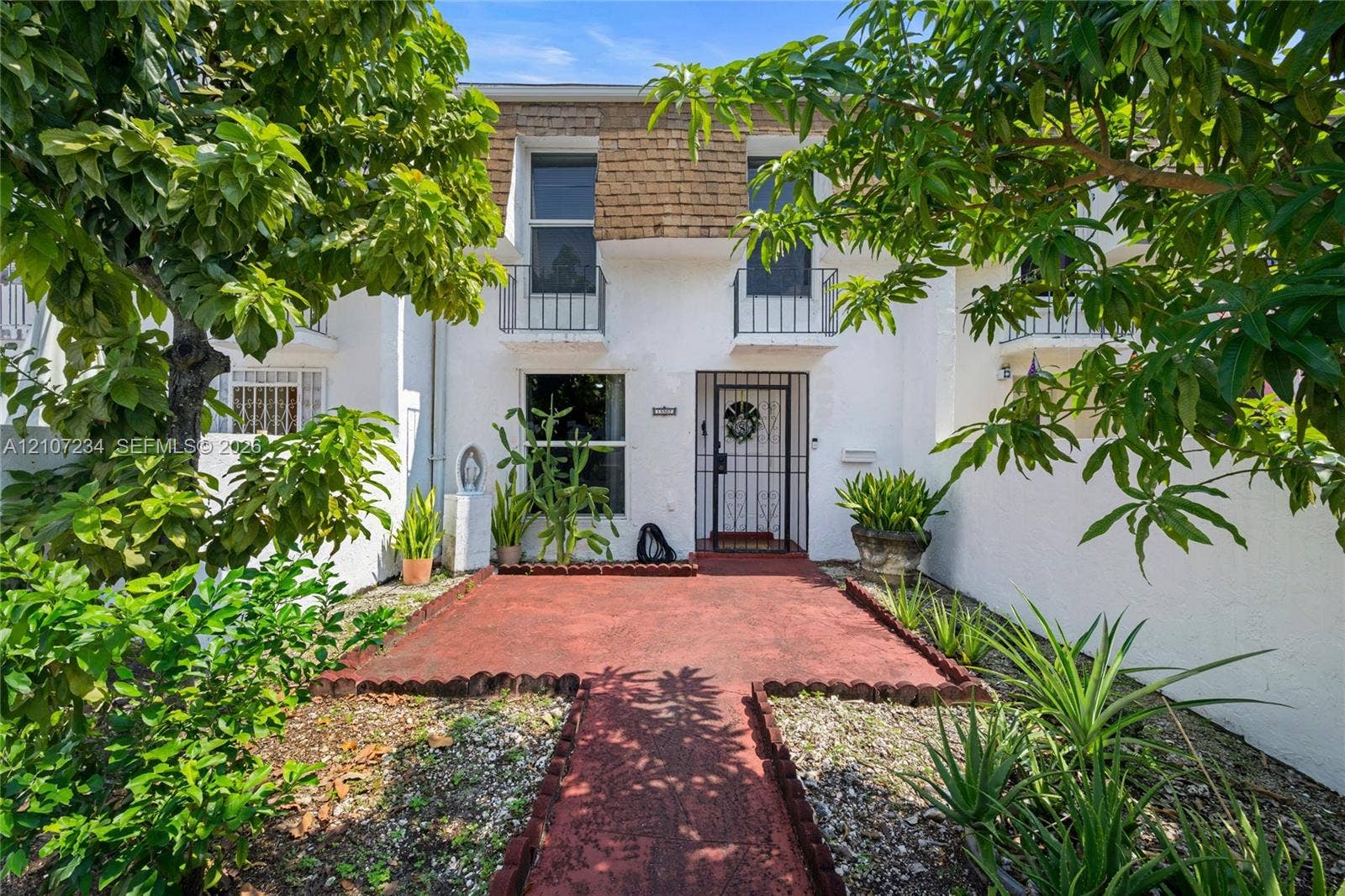 13507 NE 24th Court, North Miami, FL 33181 Exterior facade featuring white stucco finish, second-story decorative iron balcony railings, a metal security door, and a painted masonry walkway