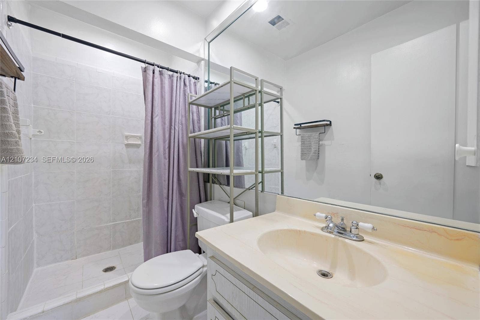 13507 NE 24th Court, North Miami, FL 33181 Bathroom featuring a vanity with integrated sink, expansive wall-mounted mirror, white ceramic tile shower surround, and polished chrome hardware