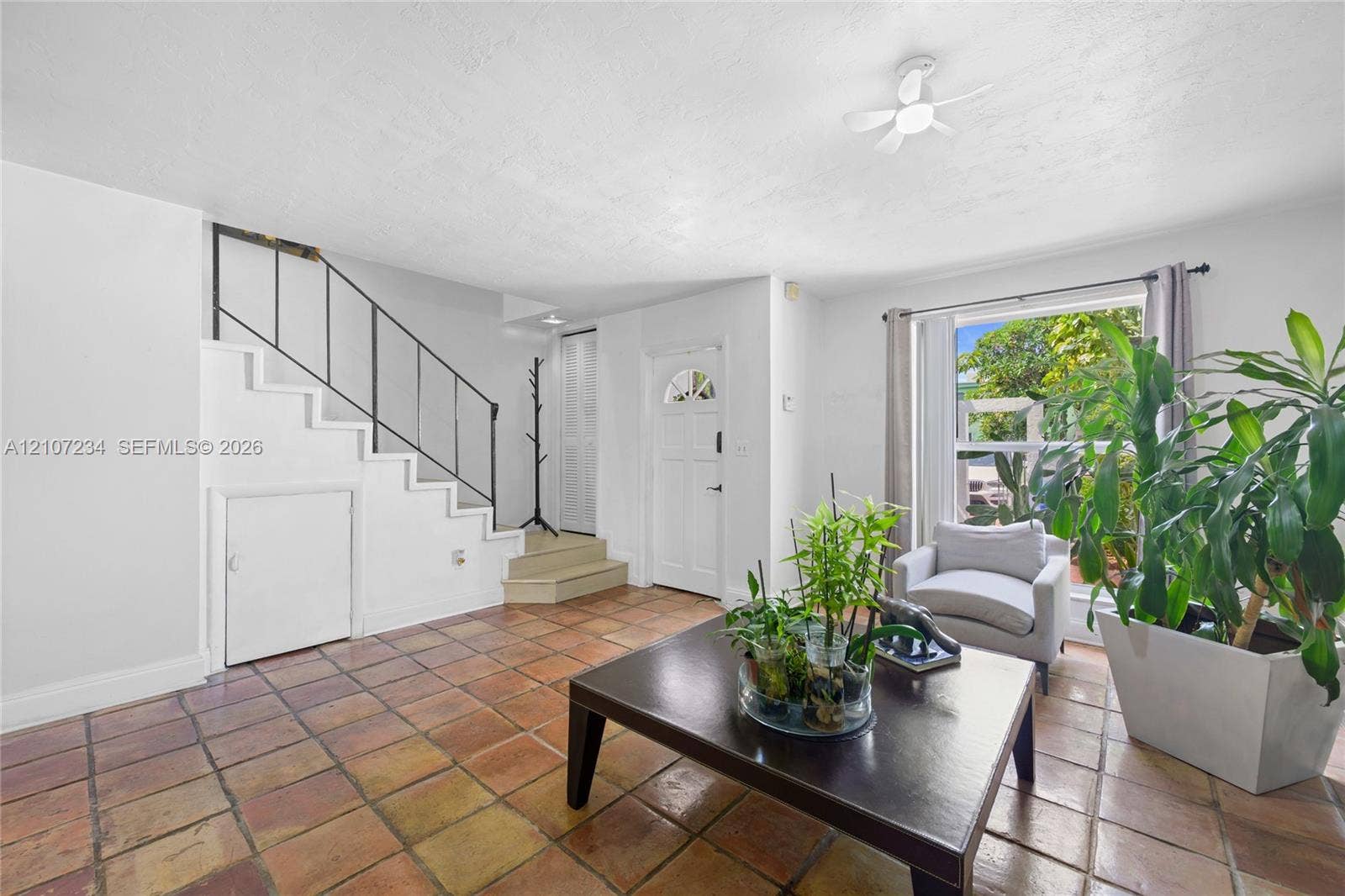 13507 NE 24th Court, North Miami, FL 33181 Terracotta tile flooring, staircase with metal railing, white-paneled front door with a half-moon window, and large window with natural light