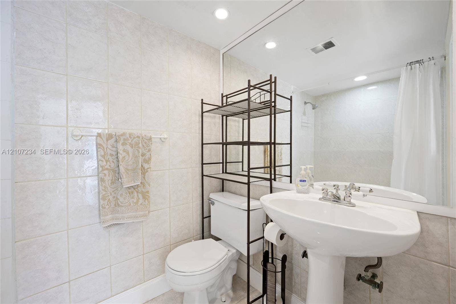 13507 NE 24th Court, North Miami, FL 33181 Bathroom featuring full-wall tile surround, pedestal sink with chrome-finish faucet, and oversized wall-mounted mirror