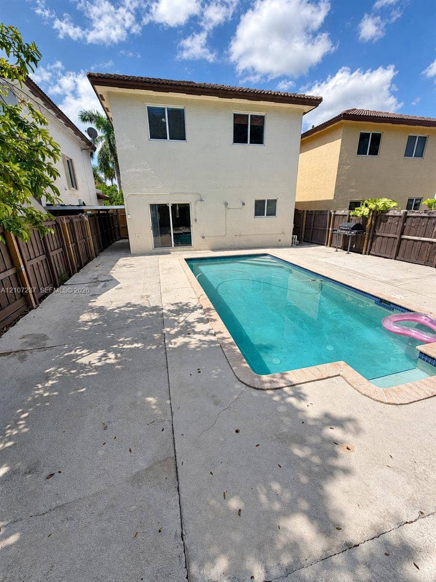 2529 NE 41st Terrace, Homestead, FL 33033 Rear exterior featuring a rectangular inground swimming pool, concrete patio, and wood privacy fencing