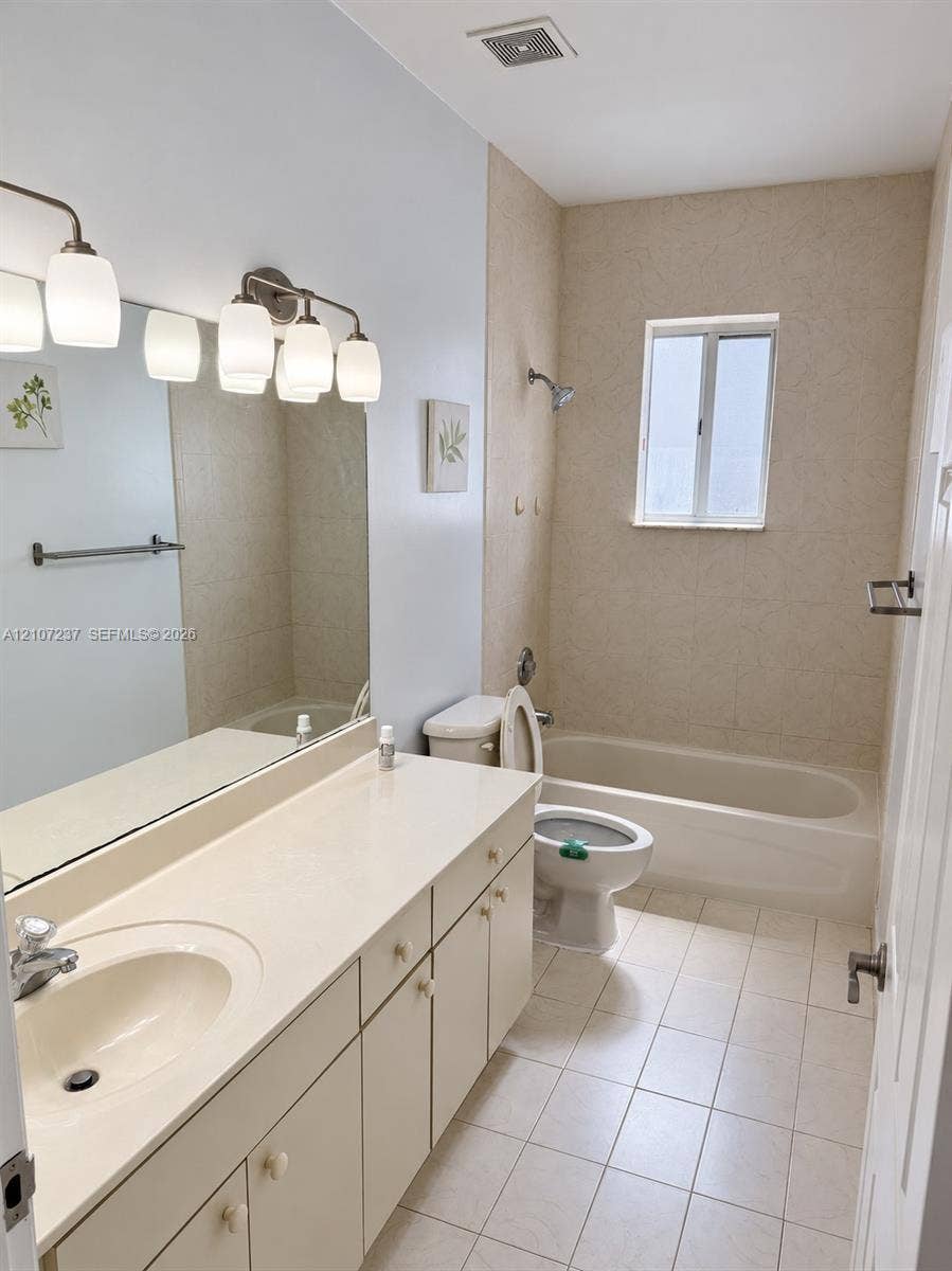 2529 NE 41st Terrace, Homestead, FL 33033 Bathroom featuring a large vanity with integrated countertop, wall-to-wall mirror, multi-light fixture, tile flooring, and a tiled tub-shower combination