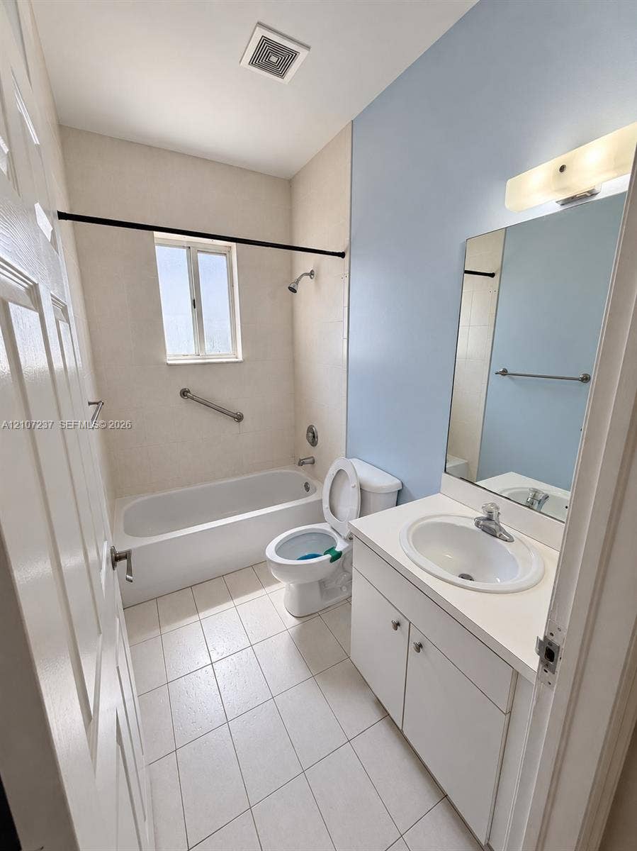 2529 NE 41st Terrace, Homestead, FL 33033 Bathroom featuring a white porcelain tub with an integrated shower, vanity cabinet with an inset sink, solid-surface countertop, and large wall-mounted mirror