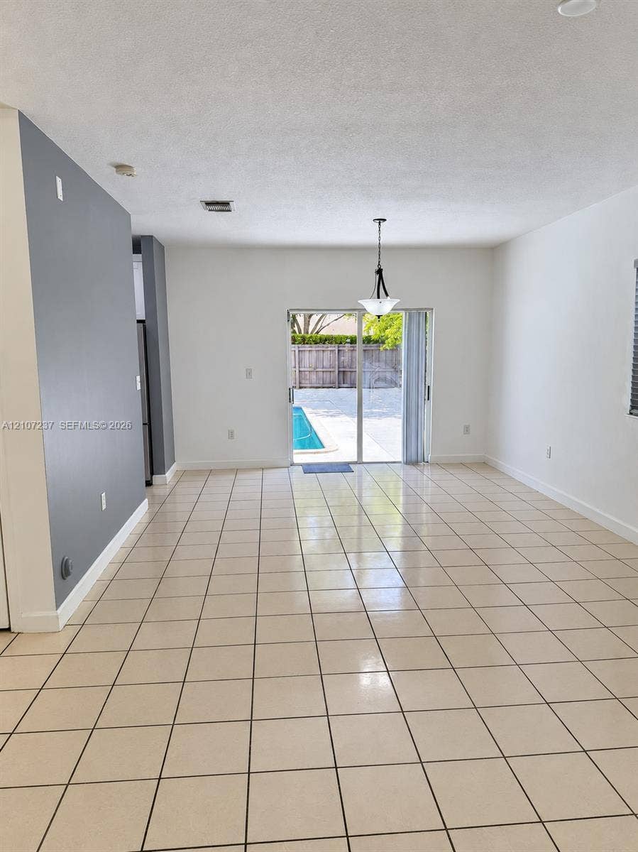 2529 NE 41st Terrace, Homestead, FL 33033 Neutral-tone interior featuring ceramic tile flooring, a dark-toned accent wall, a tiered hanging light fixture, and sliding glass doors opening to an exterior pool area