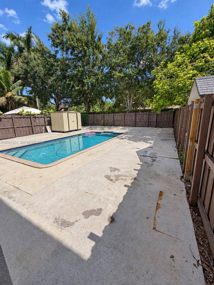 2529 NE 41st Terrace, Homestead, FL 33033 Inground swimming pool with concrete decking, enclosed by a full-height wood privacy fence, featuring mature perimeter trees