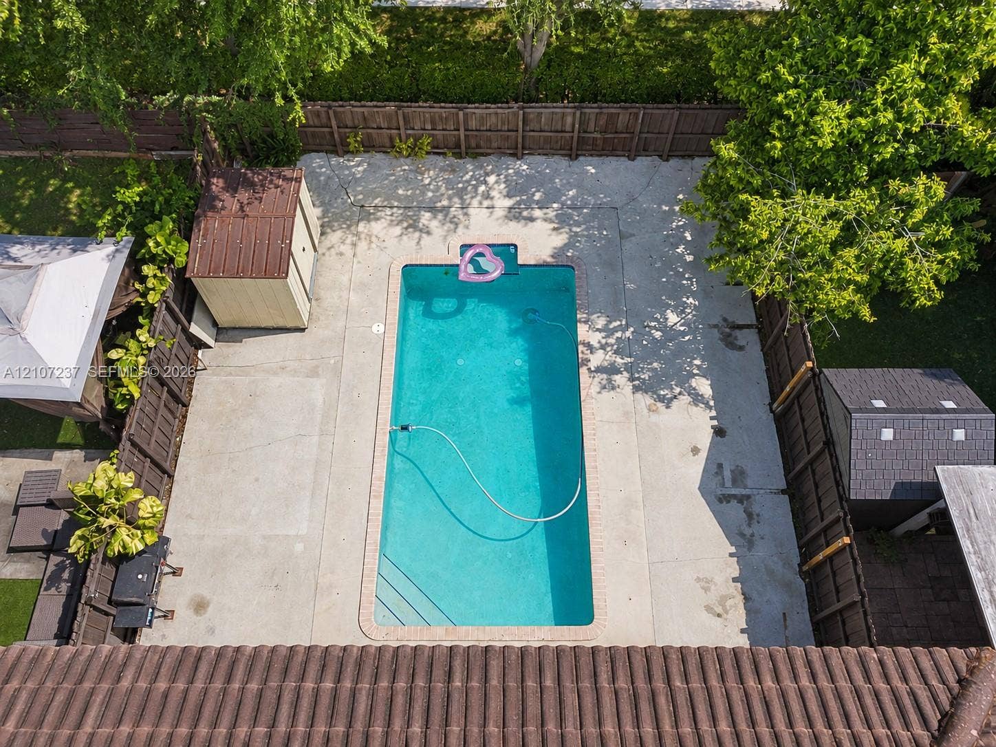 2529 NE 41st Terrace, Homestead, FL 33033 In-ground rectangular swimming pool with concrete patio surround, enclosed by a wood privacy fence and featuring two detached storage structures