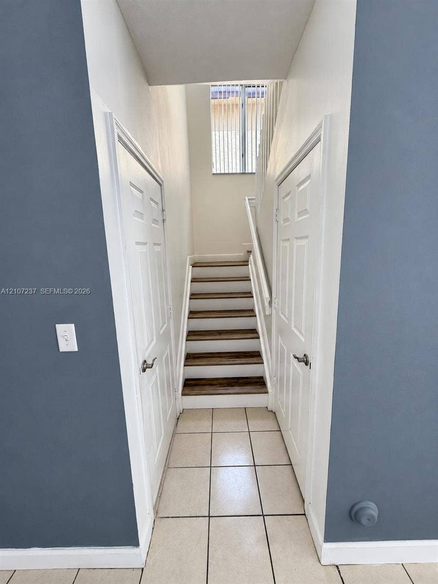 2529 NE 41st Terrace, Homestead, FL 33033 Staircase featuring wood-finish treads, white risers, and a matching handrail, flanked by two six-panel doors and finished with ceramic tile flooring