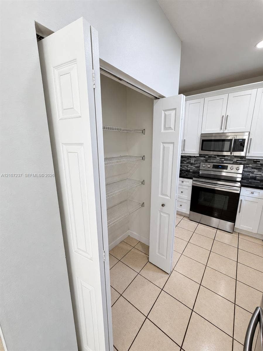 2529 NE 41st Terrace, Homestead, FL 33033 Pantry featuring wire shelving and bi-fold doors, complemented by kitchen cabinetry with stainless steel appliances, a multi-tonal backsplash, and ceramic tile flooring