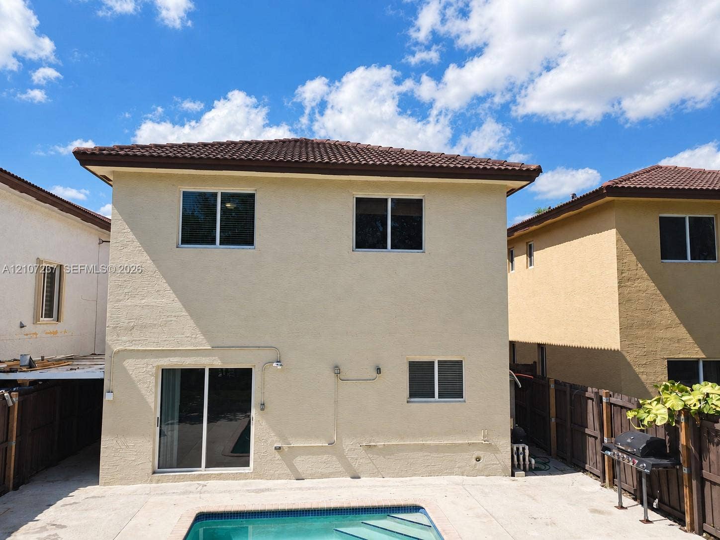 2529 NE 41st Terrace, Homestead, FL 33033 Two-story stucco exterior featuring a hipped tile roof, integrated sliding glass door, and an in-ground swimming pool with concrete decking