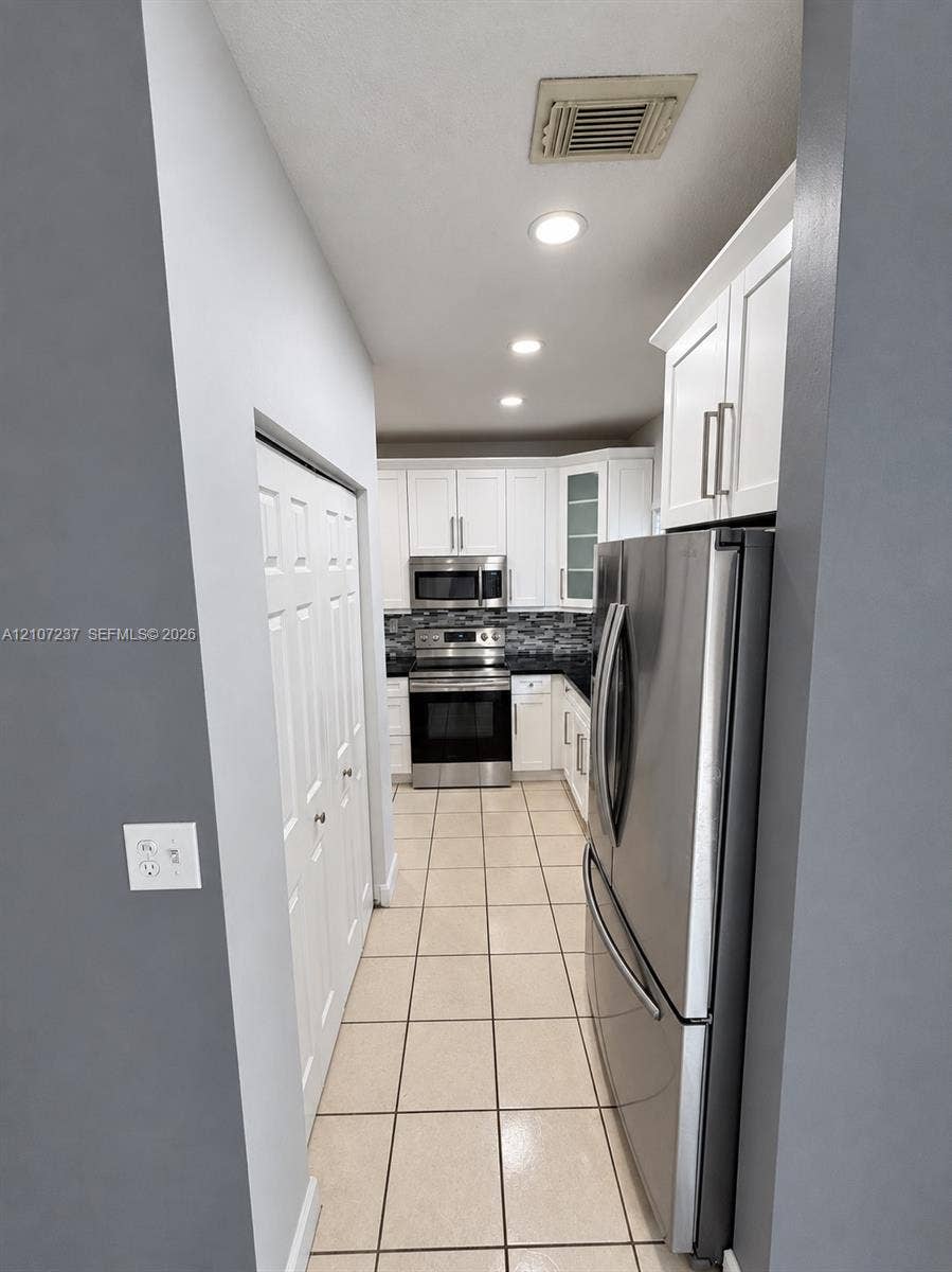 2529 NE 41st Terrace, Homestead, FL 33033 Kitchen featuring white shaker-style cabinetry, stainless steel appliances, tile flooring, and a multi-toned mosaic tile backsplash