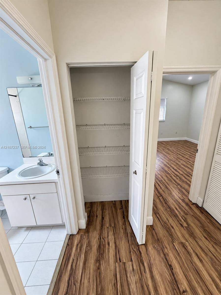 2529 NE 41st Terrace, Homestead, FL 33033 Vanity featuring a white cabinet, integrated sink, and wall-mounted mirror, paired with a reach-in closet containing multi-level wire shelving and wood-finish flooring