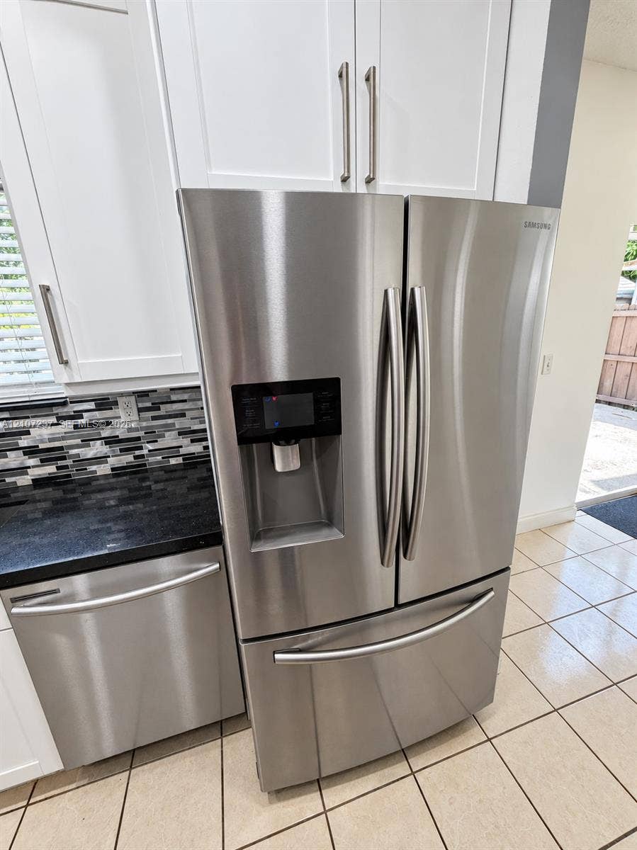 2529 NE 41st Terrace, Homestead, FL 33033 Stainless steel French door refrigerator, white shaker-style cabinetry, dark stone countertop, multi-tonal glass tile backsplash, and ceramic tile flooring