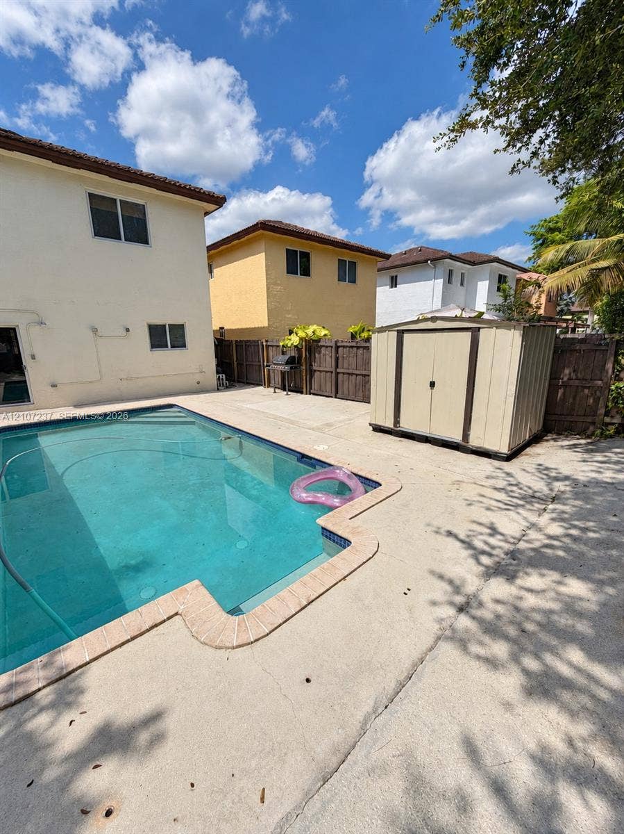 2529 NE 41st Terrace, Homestead, FL 33033 In-ground swimming pool with stone coping, expansive concrete patio, and detached storage structure, enclosed by a wood privacy fence