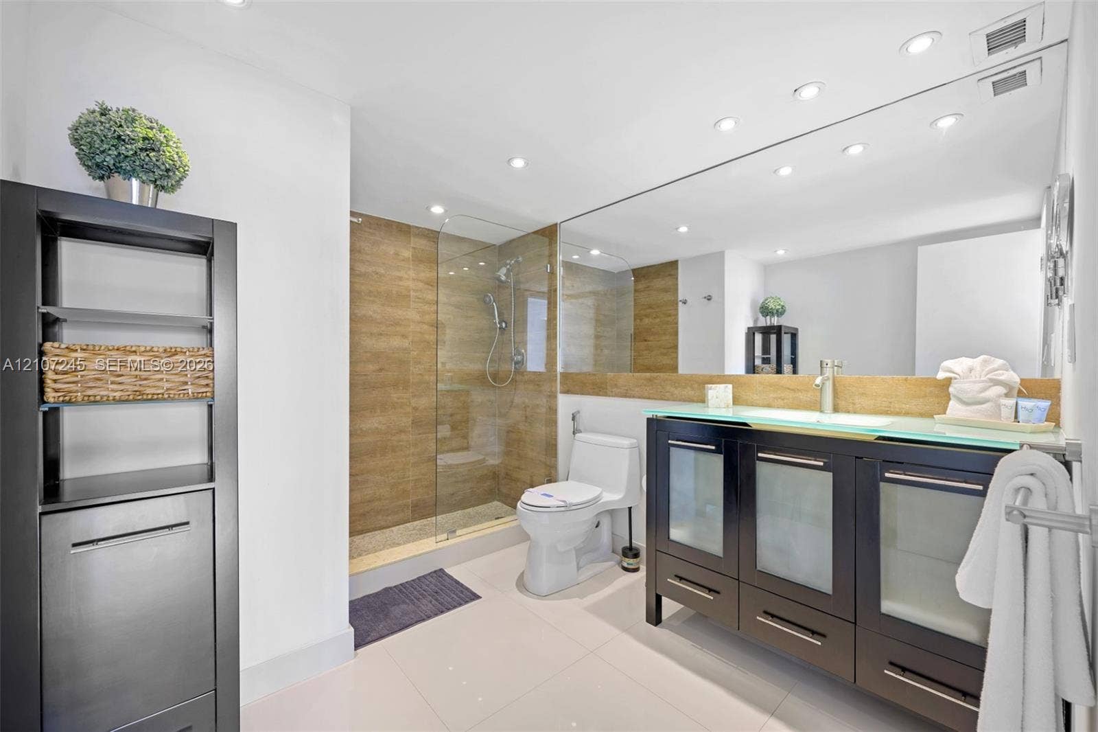 19370 Collins Avenue, #PH-14, Sunny Isles Beach, Sunny Isles Beach, FL 33160 Bathroom featuring a vanity with frosted glass cabinet doors and a glass countertop, a walk-in shower with floor-to-ceiling tile, and a large-format mirror