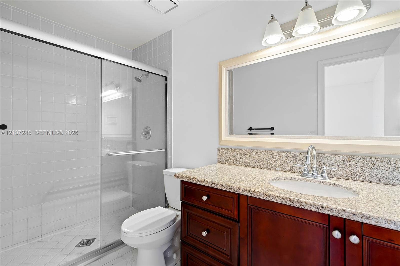 9983 W Atlantic Boulevard, #9983, Coral Springs, Coral Springs, FL 33071 Bathroom vanity with dark wood-finish cabinetry, stone-composite countertop, oval undermount sink, three-light fixture, and glass-enclosed shower with tiled surround