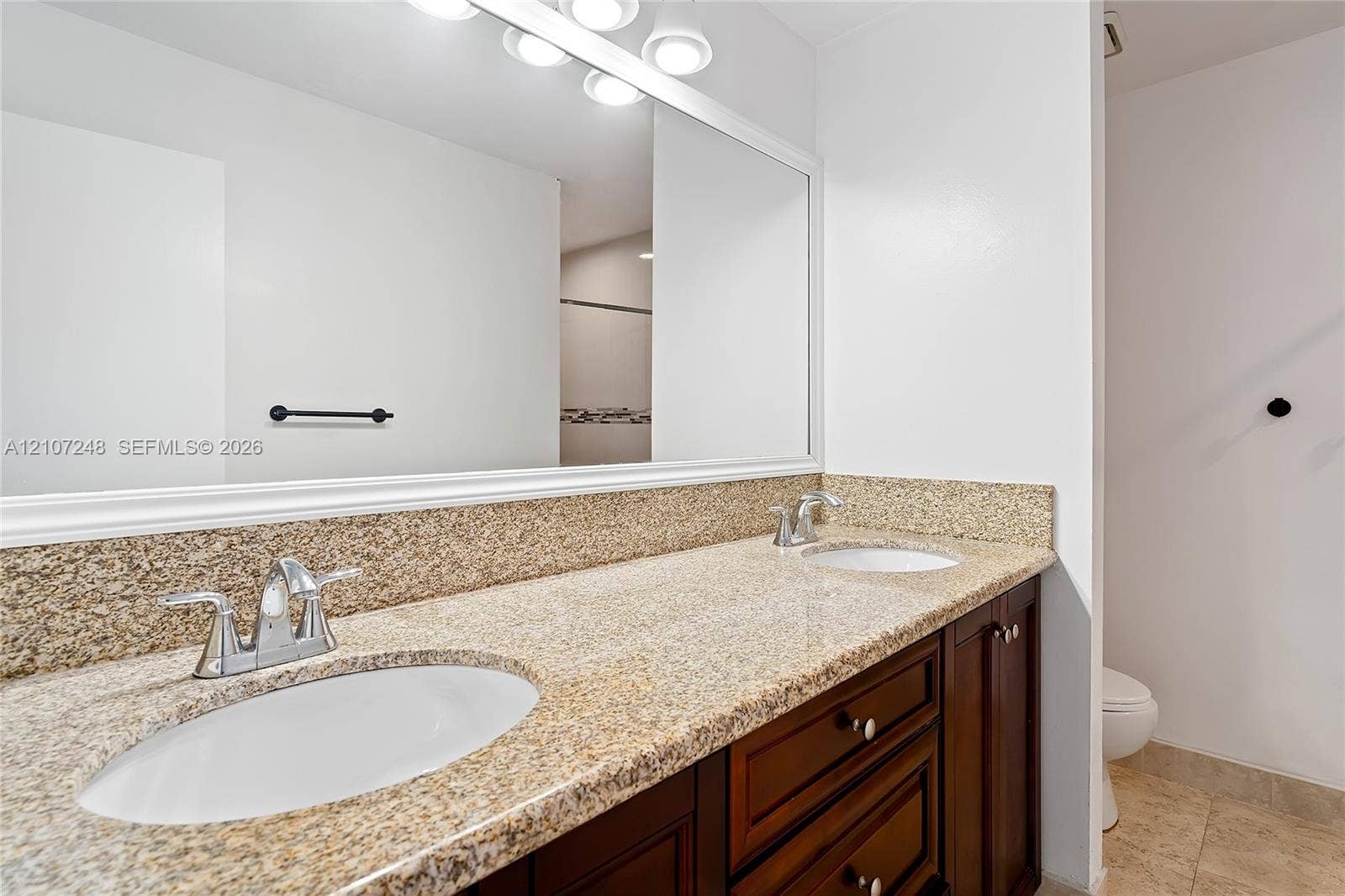 9983 W Atlantic Boulevard, #9983, Coral Springs, Coral Springs, FL 33071 Dual-sink vanity featuring stone-finish countertops, warm-toned wood cabinetry, polished chrome faucets, and a full-width wall mirror with integrated lighting