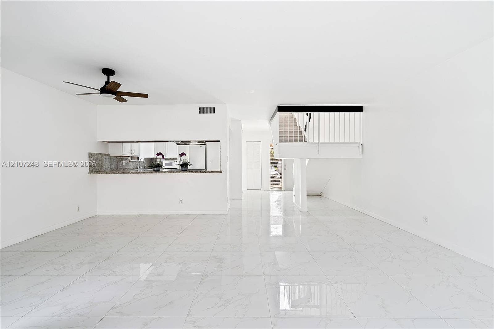 9983 W Atlantic Boulevard, #9983, Coral Springs, Coral Springs, FL 33071 Open-concept living space featuring high-gloss tile flooring, an integrated kitchen peninsula with stone-finish countertops, a dark-finish ceiling fan, and a staircase with white vertical balusters