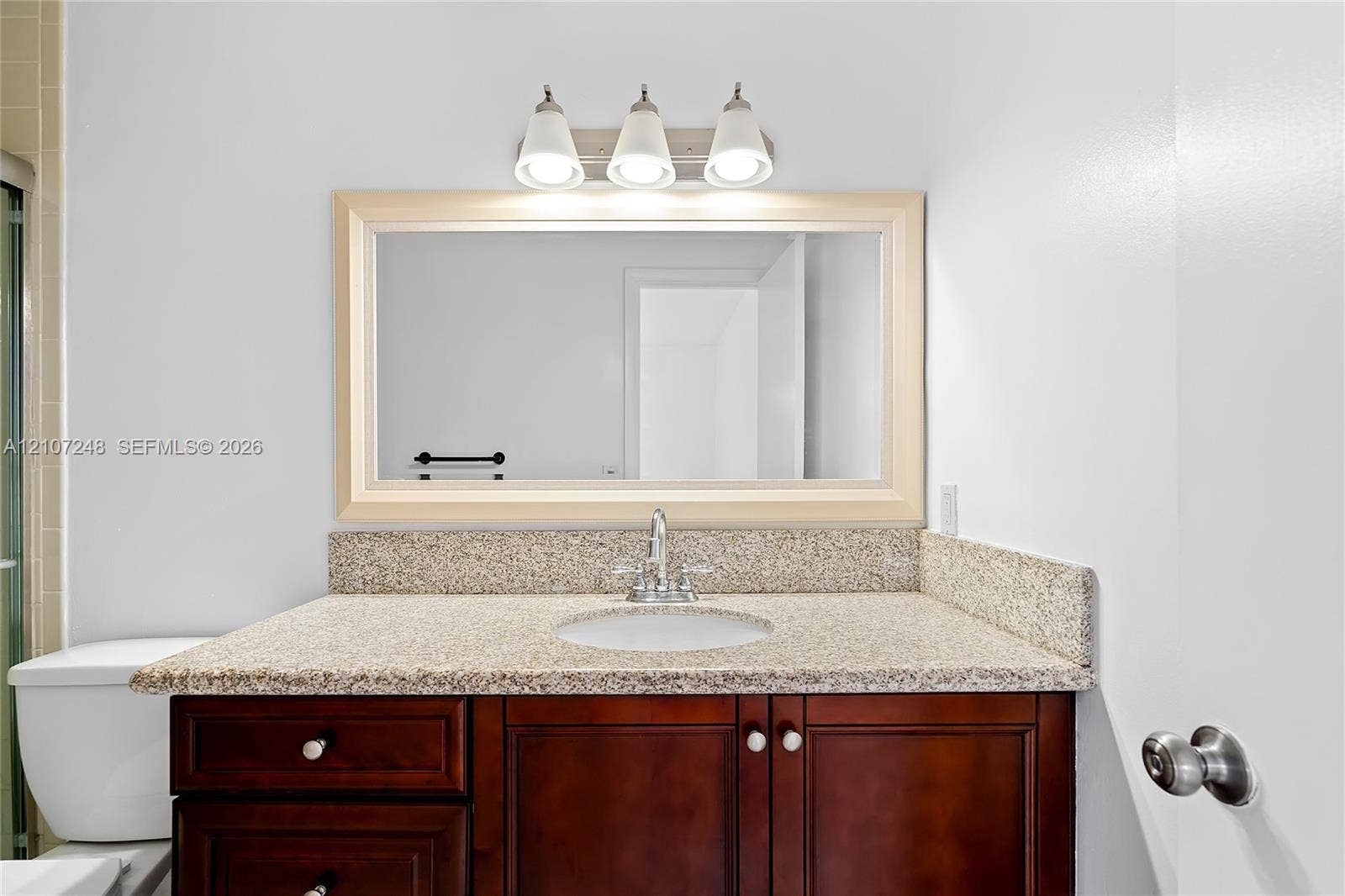 9983 W Atlantic Boulevard, #9983, Coral Springs, Coral Springs, FL 33071 Vanity featuring a dark-finish wood cabinet, stone-surface countertop with an integrated basin, three-light fixture, and a framed mirror
