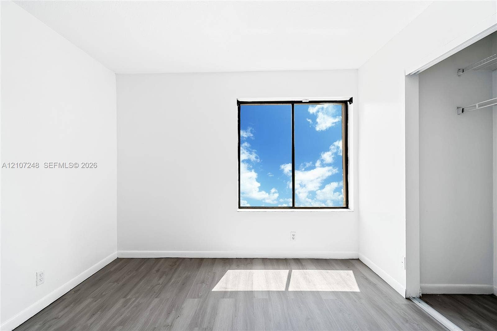 9983 W Atlantic Boulevard, #9983, Coral Springs, Coral Springs, FL 33071 Neutral-toned wood-finish flooring, white walls, and a large window with sliding glass panels, complemented by a built-in closet with integrated shelving
