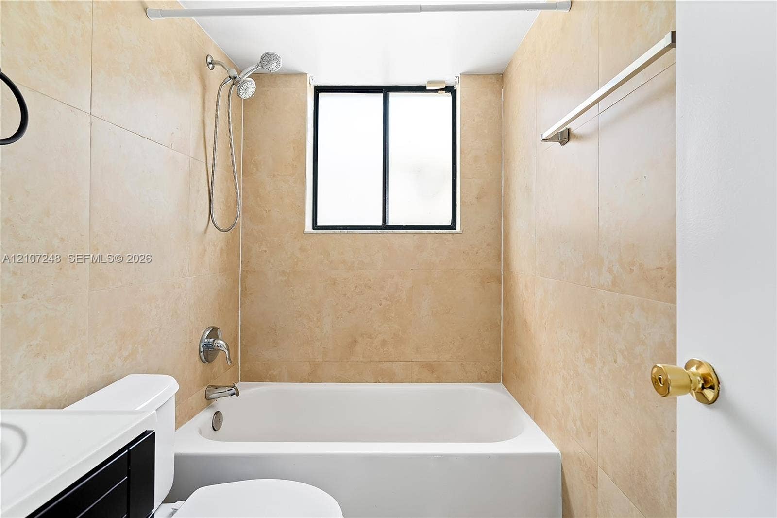 9983 W Atlantic Boulevard, #9983, Coral Springs, Coral Springs, FL 33071 Full-height neutral stone-style wall tile, white soaking tub, handheld shower fixture, black-framed window, and metallic finish towel bar