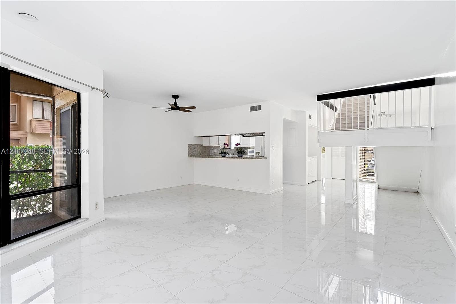 9983 W Atlantic Boulevard, #9983, Coral Springs, Coral Springs, FL 33071 Open-concept interior featuring large-format polished tile flooring, a pass-through kitchen window with stone-finish countertops, and an elevated metal staircase railing