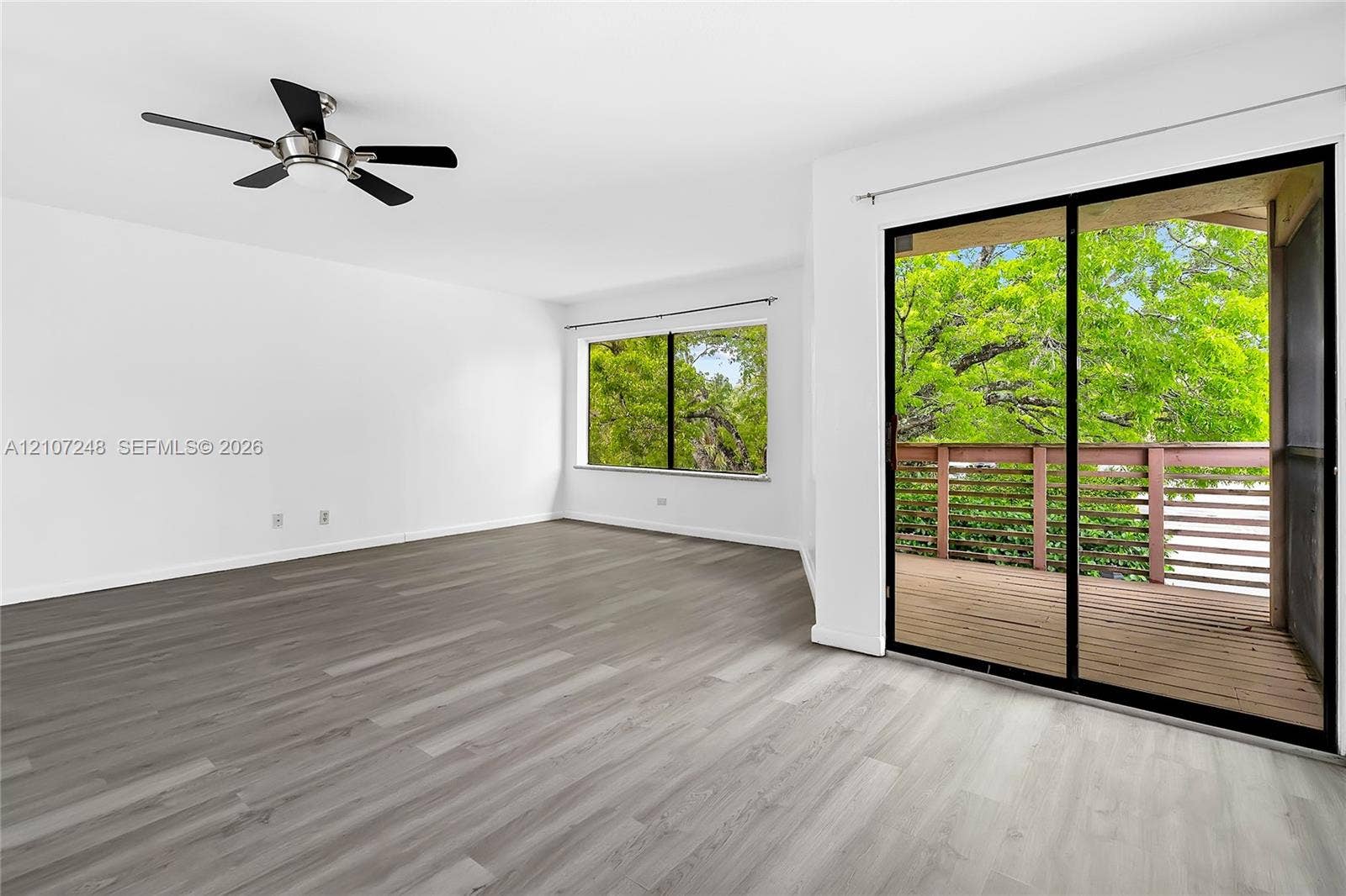 9983 W Atlantic Boulevard, #9983, Coral Springs, Coral Springs, FL 33071 Living area featuring wood-finish flooring, a ceiling fan with integrated lighting, oversized windows, and sliding glass doors opening to a wood-decked balcony