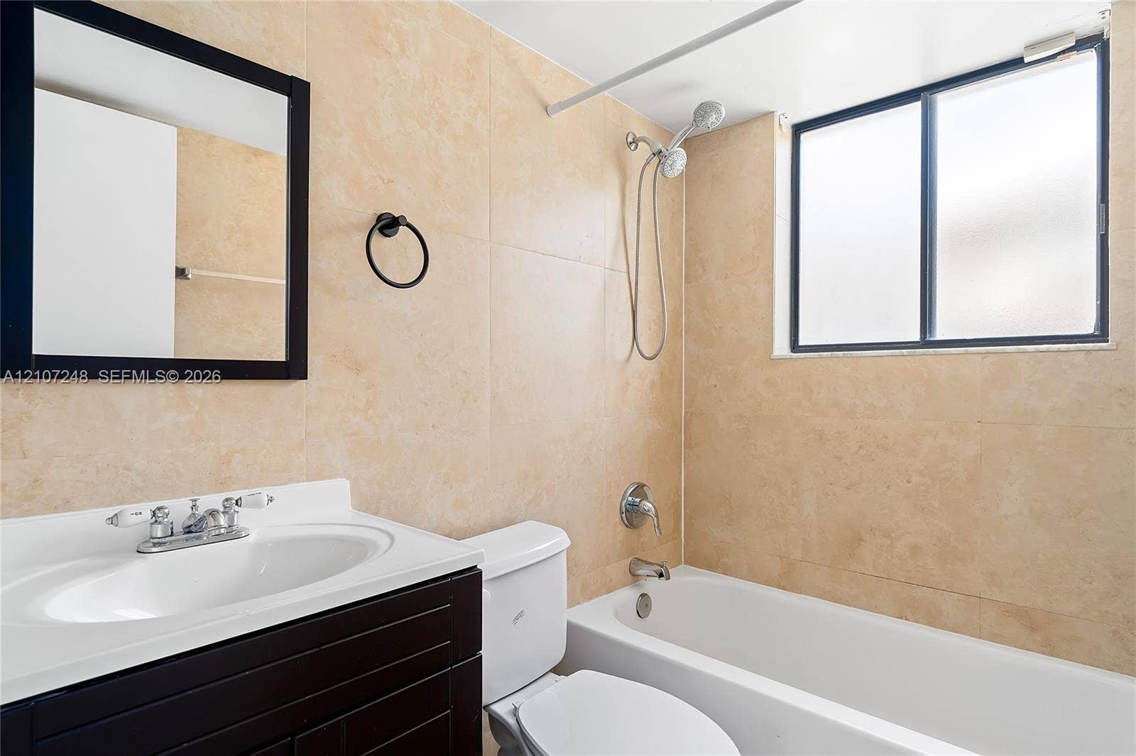 9983 W Atlantic Boulevard, #9983, Coral Springs, Coral Springs, FL 33071 Bathroom featuring a dark-finish vanity with an integrated white sink, wall-mounted black-framed mirror, neutral tile wall cladding, and a combination tub and shower with a handheld fixture