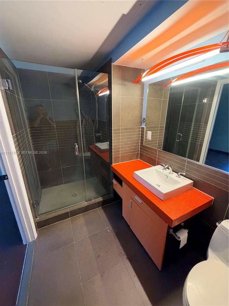 435 21st Street, #316, Miami Beach, Miami Beach, FL 33139 Bathroom featuring a glass-enclosed shower, wall-mounted vanity with a rectangular vessel sink, large-format tile flooring, and integrated wall lighting