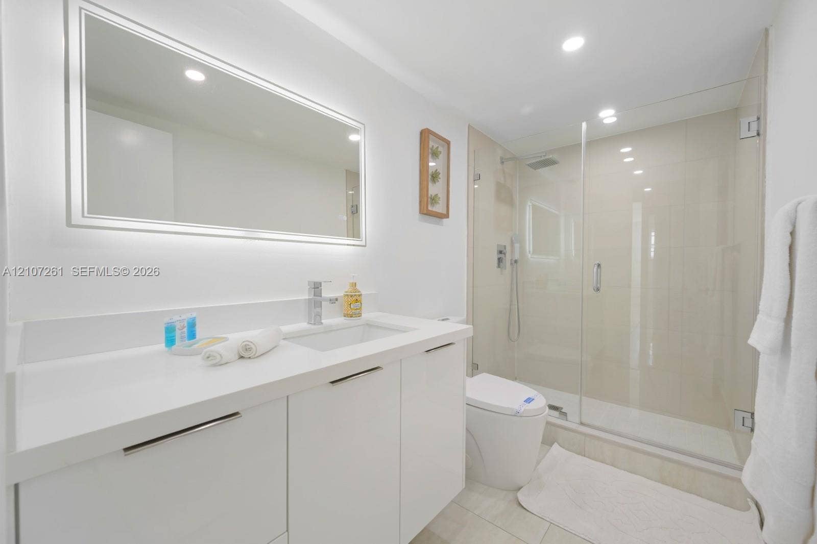 19370 Collins Avenue, #1601, Sunny Isles Beach, Sunny Isles Beach, FL 33160 Bathroom featuring a white vanity with an integrated countertop sink, an illuminated wall-mounted mirror, a walk-in shower with a glass enclosure, and recessed lighting
