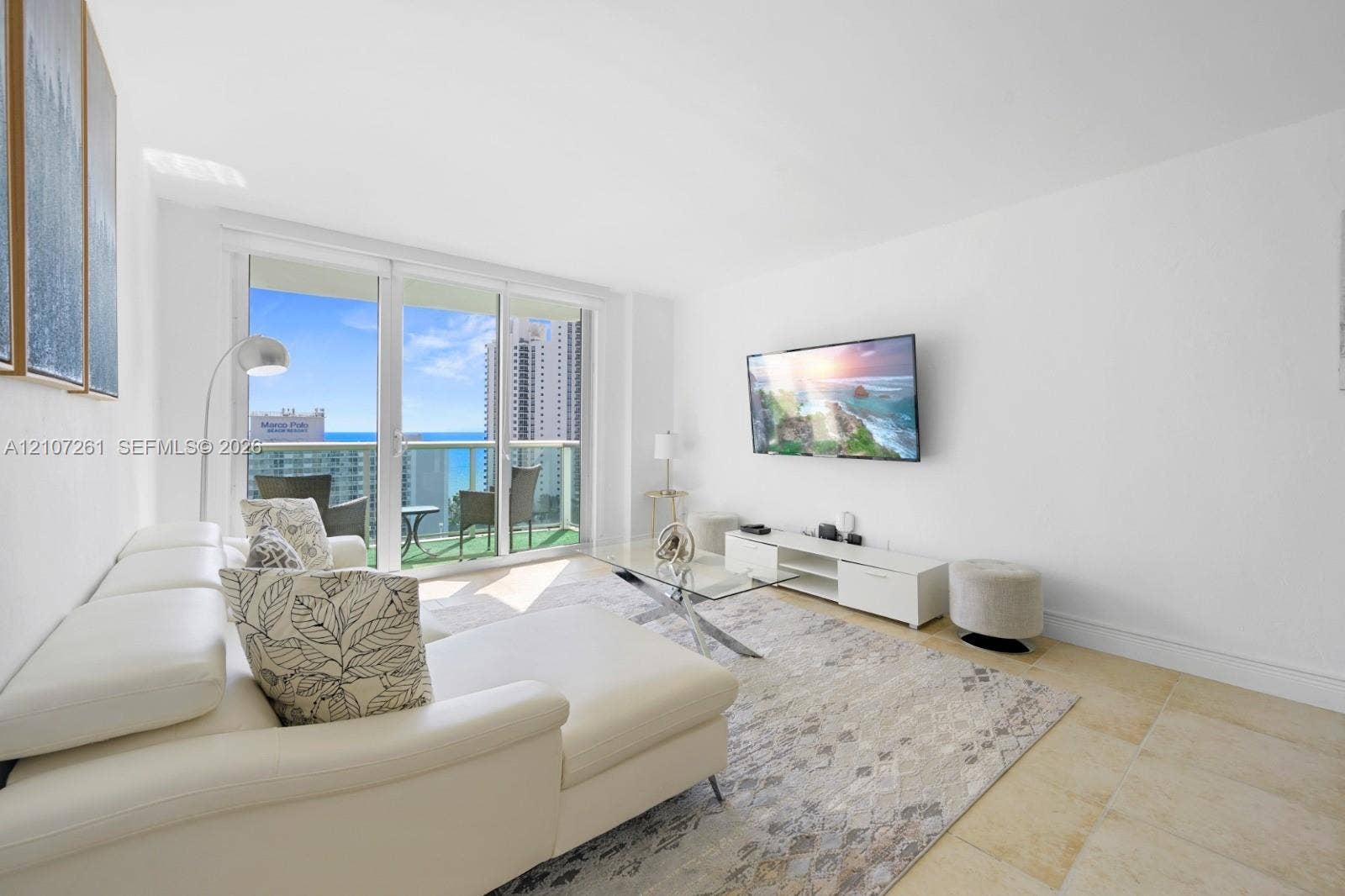 19370 Collins Avenue, #1601, Sunny Isles Beach, Sunny Isles Beach, FL 33160 Living area featuring expansive floor-to-ceiling glass sliding doors, private balcony, and light-toned stone tile flooring