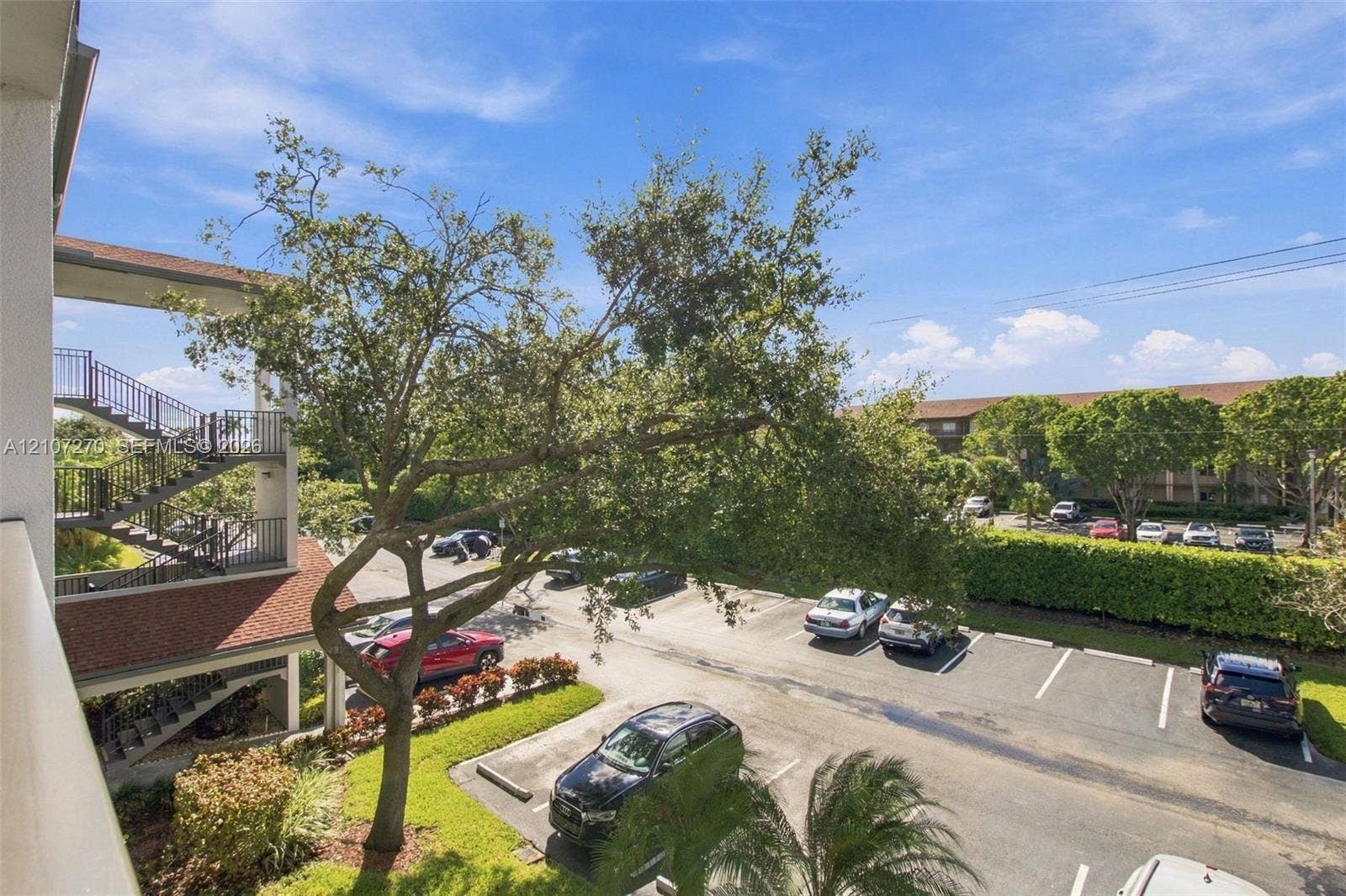 12501 SW 14th Street, #311R, Pembroke Pines, FL 33027 Exterior staircase with metal railings, mature canopy tree, and paved surface parking