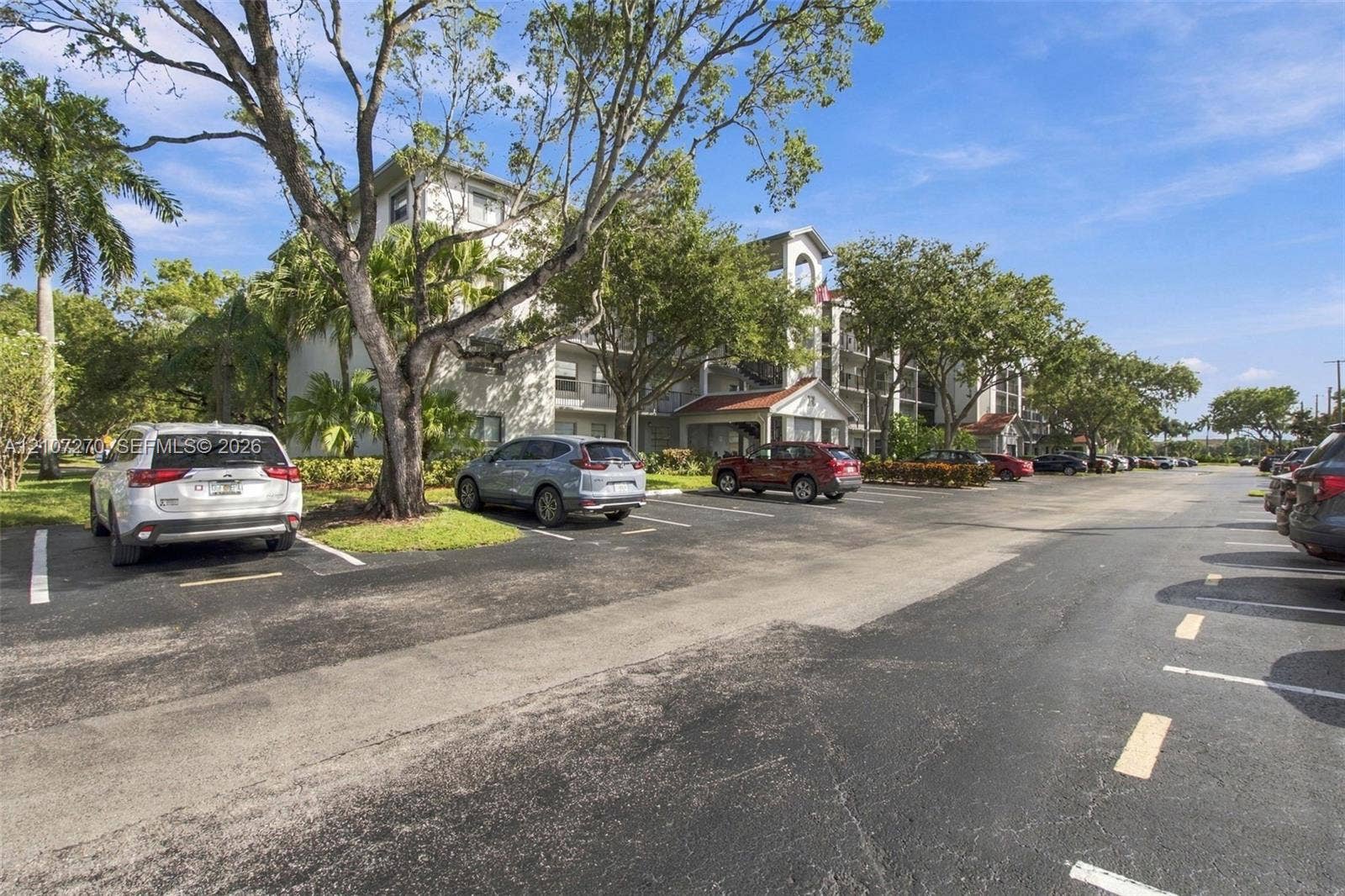 12501 SW 14th Street, #311R, Pembroke Pines, FL 33027 Multi-story building featuring stucco exterior, pitched roofline with red tile accents, covered entryway, and mature shade trees