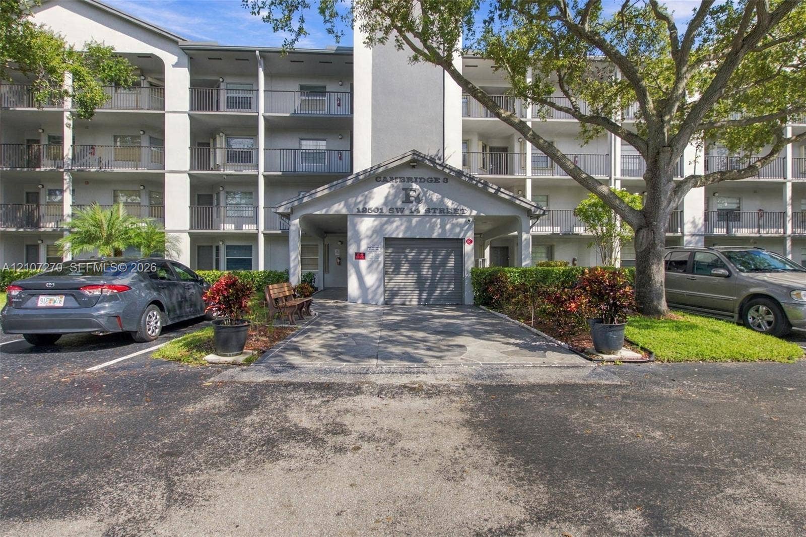 12501 SW 14th Street, #311R, Pembroke Pines, FL 33027 Multi-story exterior featuring a covered entryway, private garage, tiered balconies with metal railings, and mature landscaping