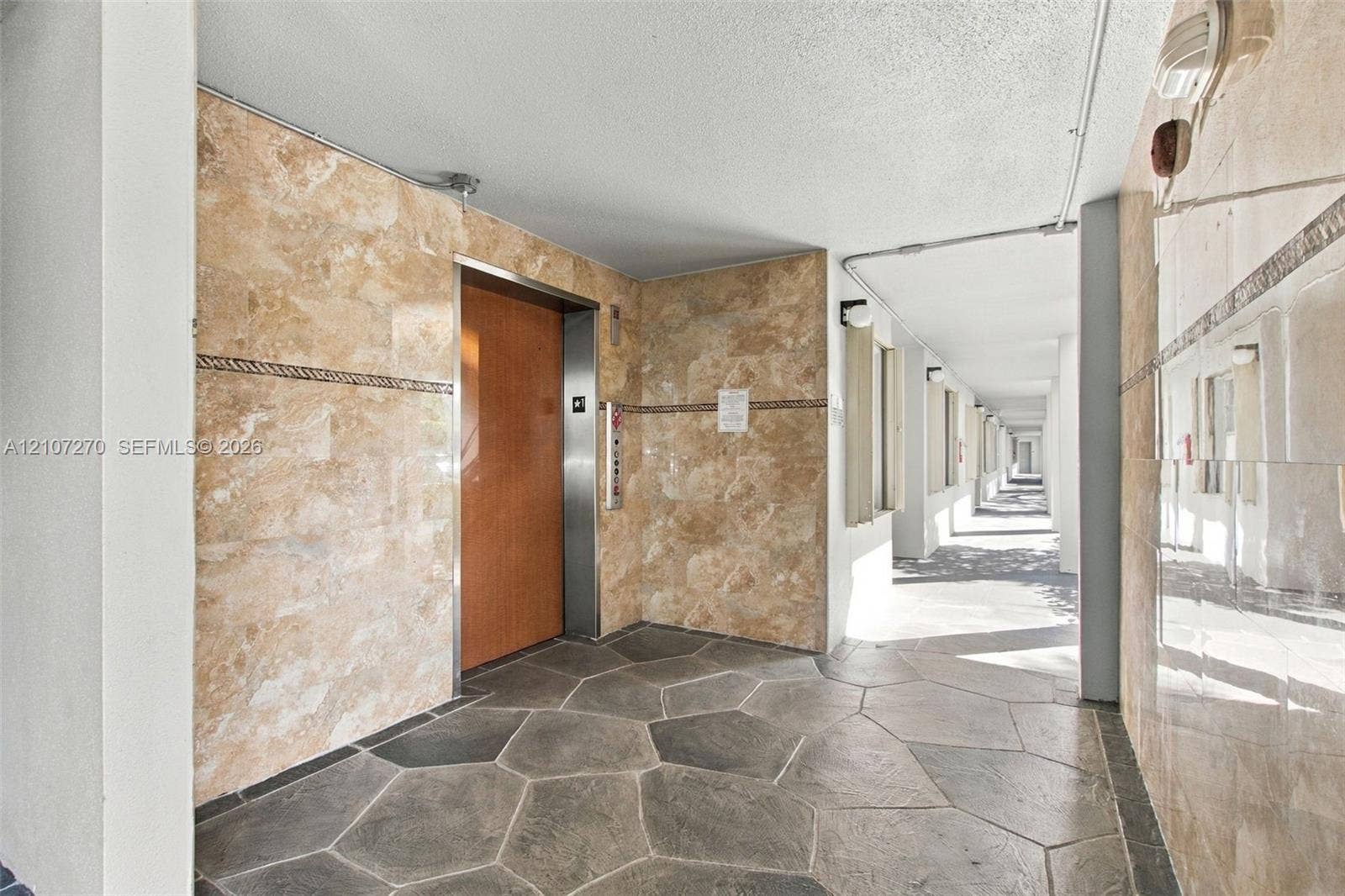 12501 SW 14th Street, #311R, Pembroke Pines, FL 33027 Elevator lobby featuring polished stone wall cladding, decorative tile border accents, and flagstone-style flooring