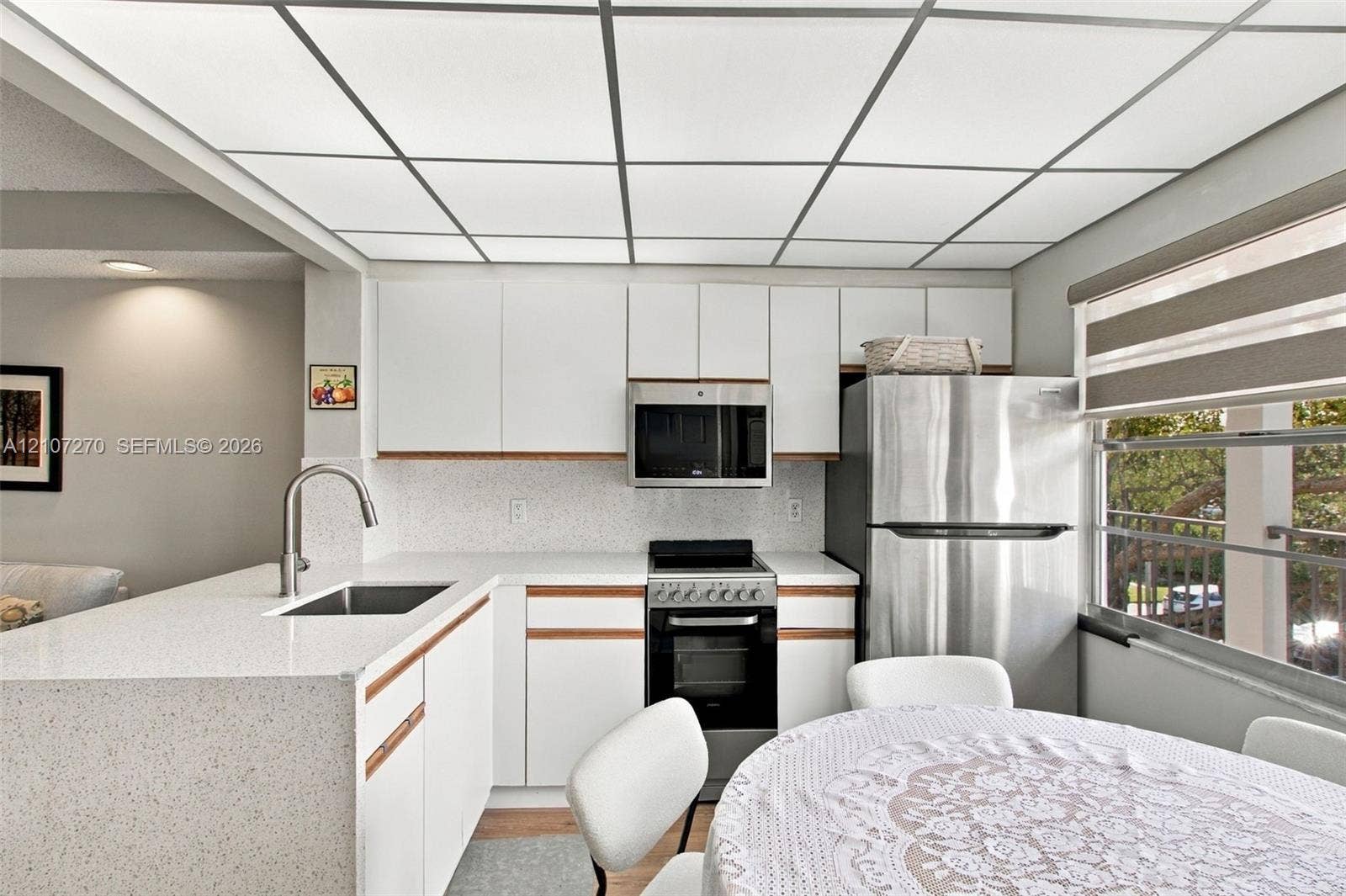 12501 SW 14th Street, #311R, Pembroke Pines, FL 33027 Kitchen featuring white flat-panel cabinetry, light-toned solid surface countertops, a stainless steel undermount sink with a gooseneck faucet, built-in stainless steel appliances, and a grid-style drop ceiling