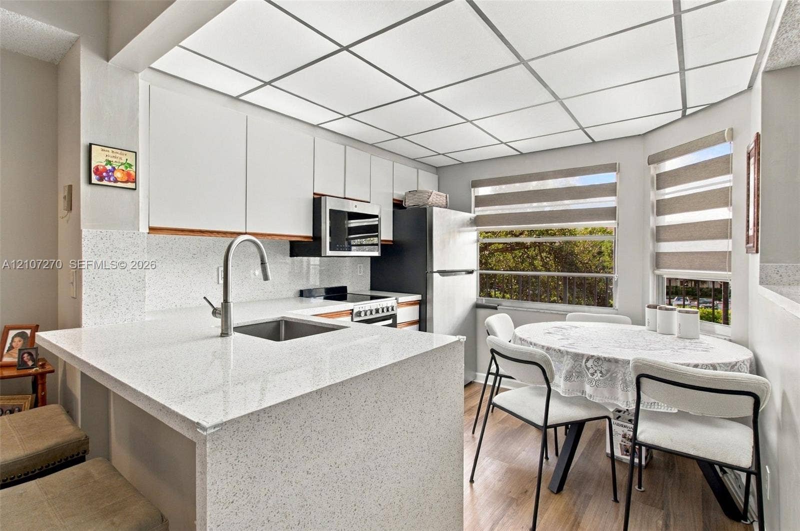 12501 SW 14th Street, #311R, Pembroke Pines, FL 33027 Kitchen featuring white flat-panel cabinetry, light-toned speckled countertops, a stainless steel undermount sink with a gooseneck faucet, wood-finish flooring, and a drop ceiling grid