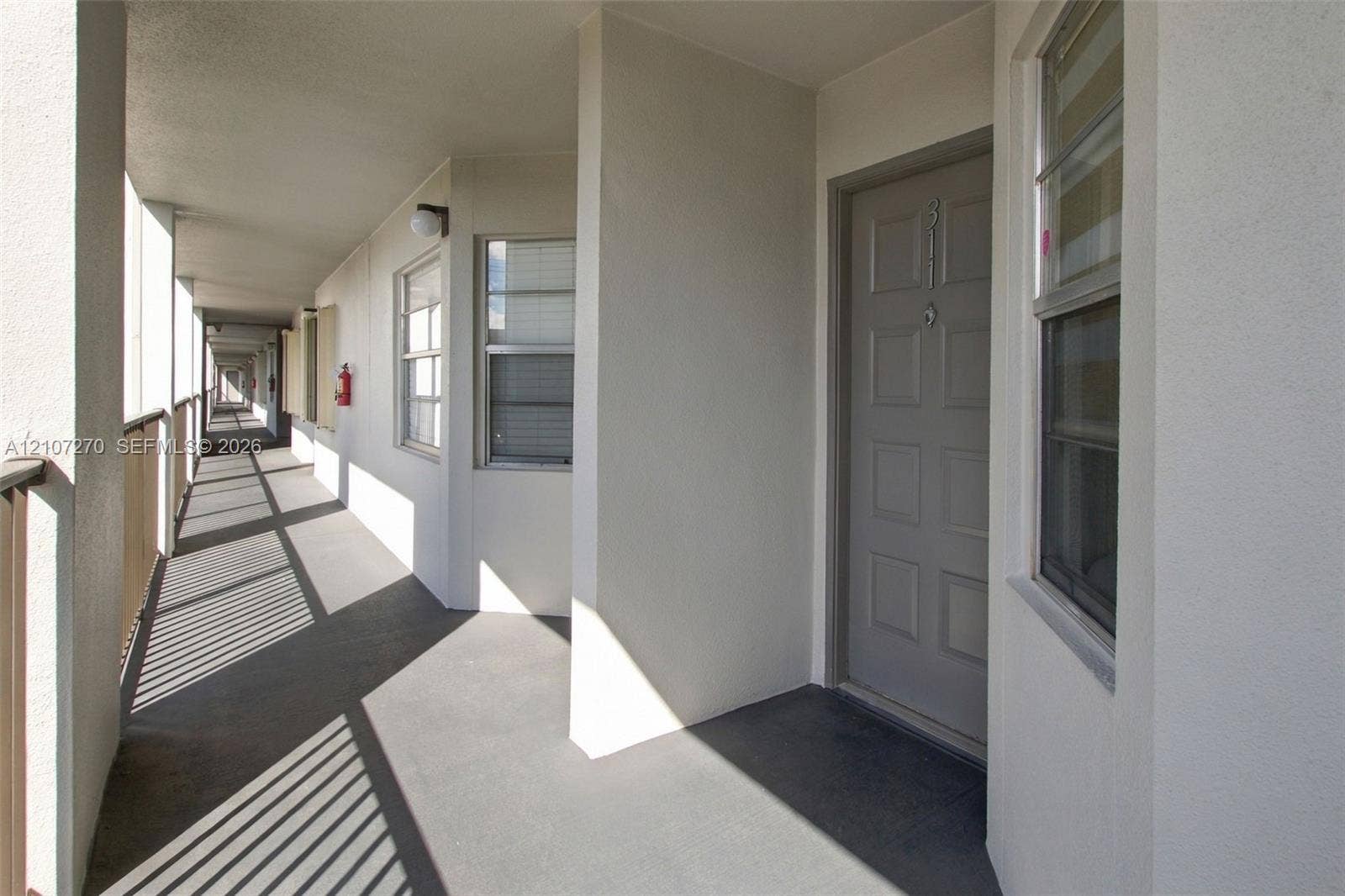 12501 SW 14th Street, #311R, Pembroke Pines, FL 33027 Exterior walkway featuring a six-panel door, neutral stucco walls, metal railings, and dual-pane windows