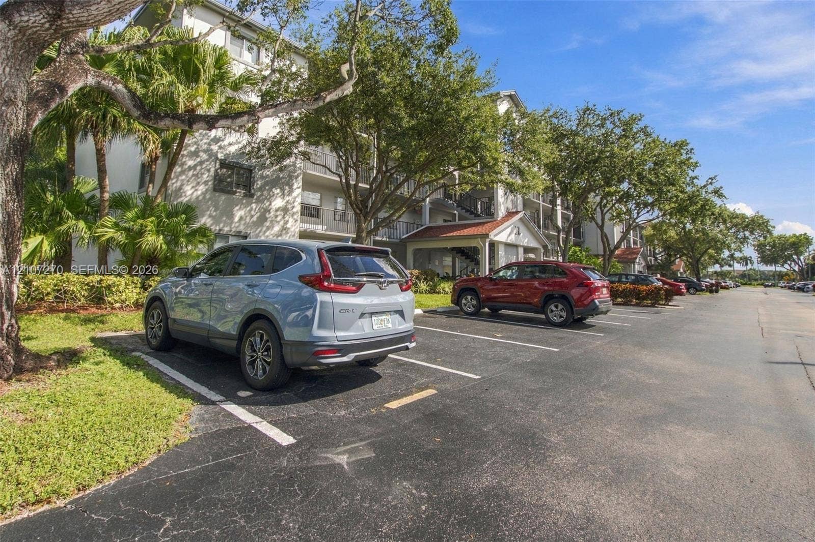 12501 SW 14th Street, #311R, Pembroke Pines, FL 33027 Multi-story residential building exterior featuring stucco cladding, balconies with metal railings, a terracotta-tiled roof portico, and dedicated surface parking