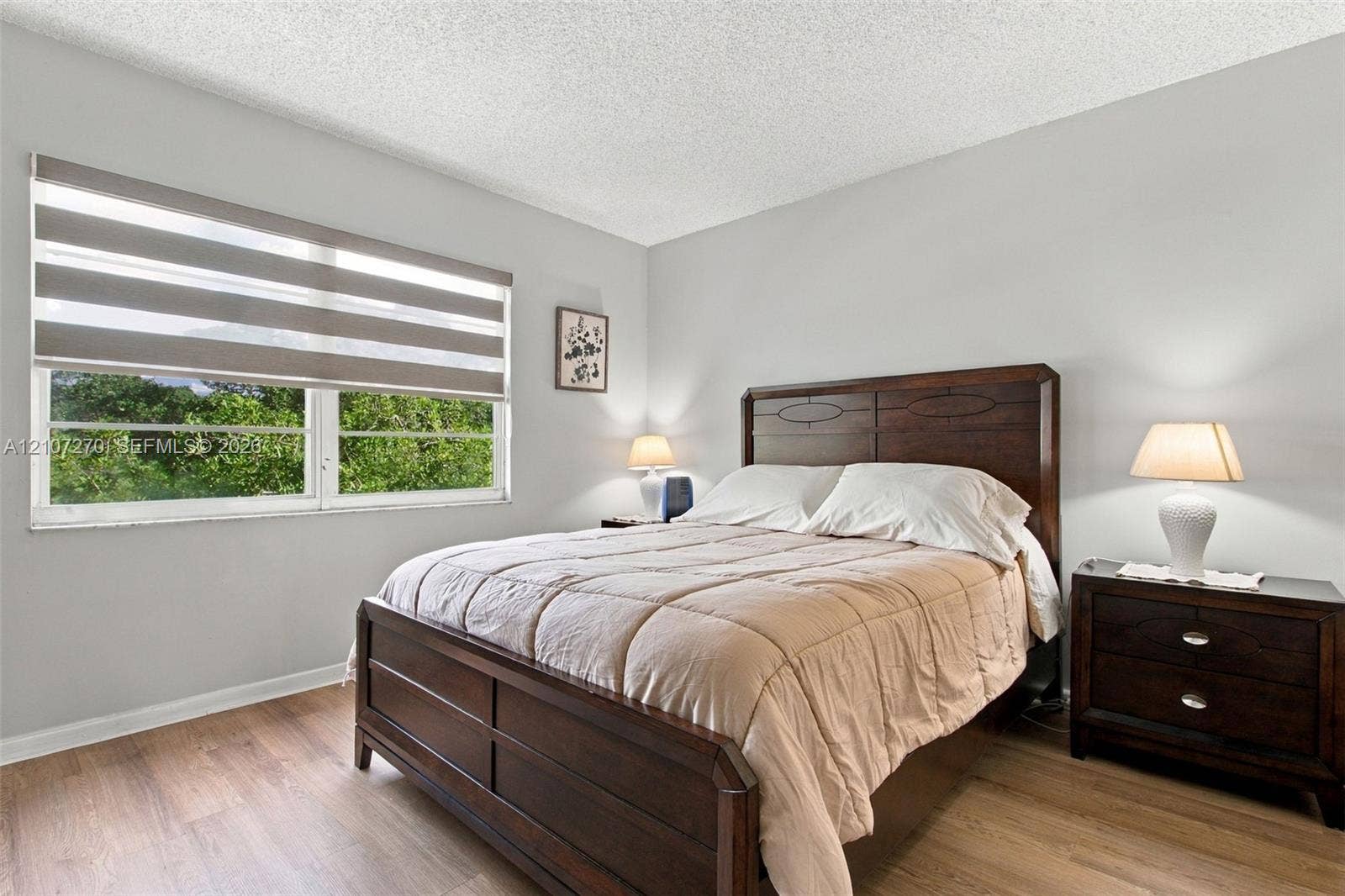 12501 SW 14th Street, #311R, Pembroke Pines, FL 33027 Bedroom featuring wood-finish flooring, textured ceiling, and large window with adjustable zebra-pattern roller shades