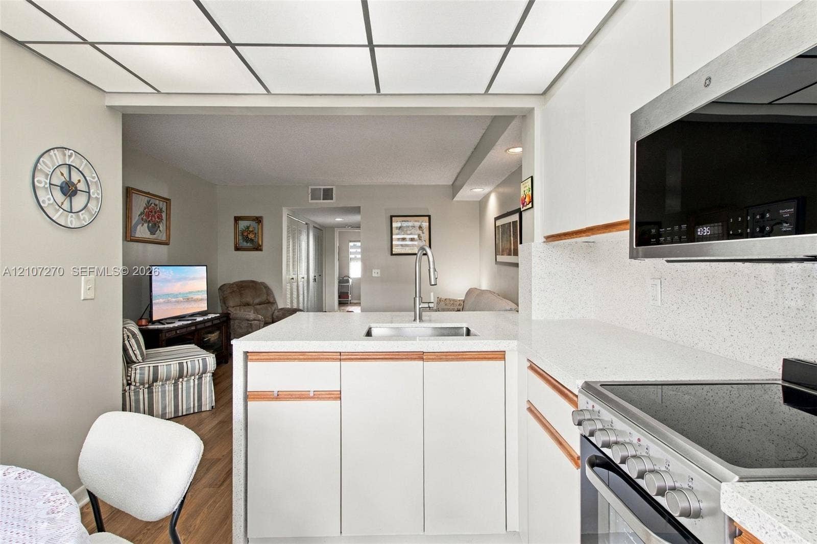 12501 SW 14th Street, #311R, Pembroke Pines, FL 33027 Kitchen featuring white cabinetry with wood-tone accents, solid surface countertops, stainless steel appliances, and a grid-style drop ceiling