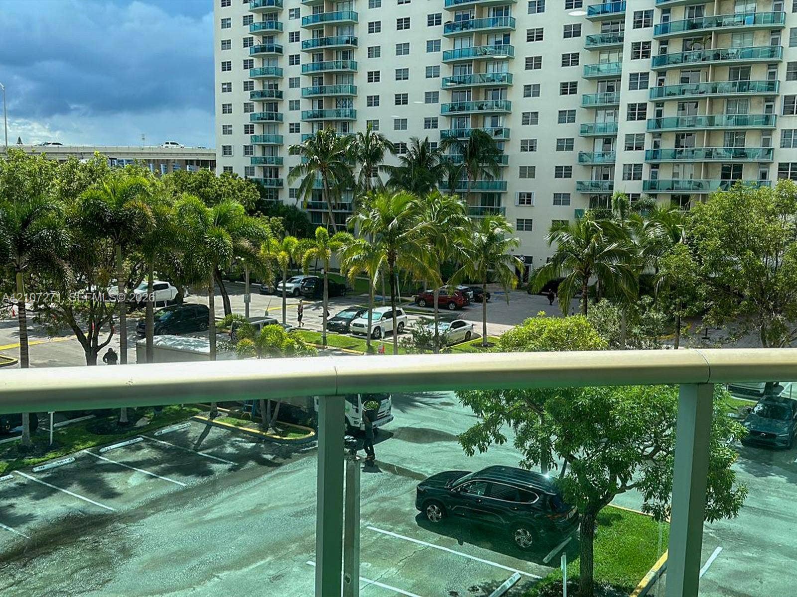 Balcony featuring a glass-panel railing, overlooking mature palm trees and landscaped grounds